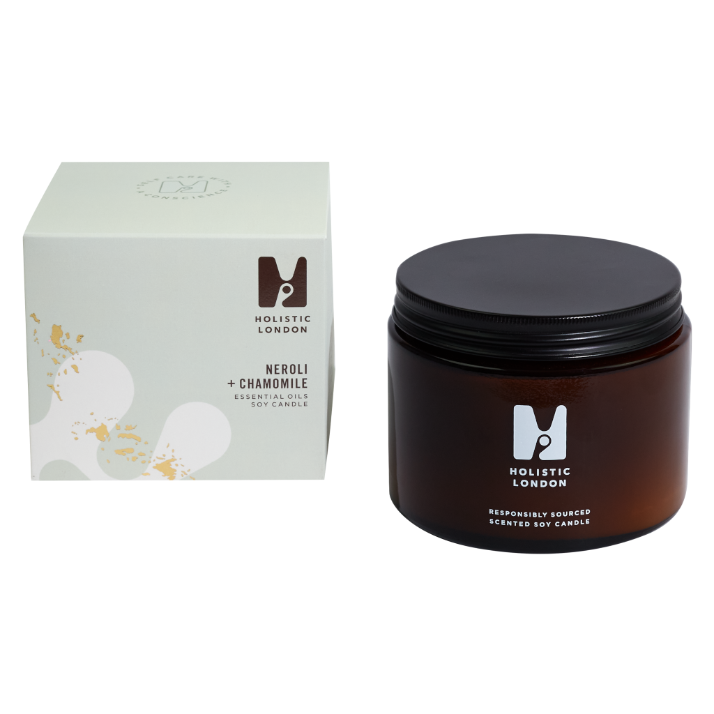 photograph of holistic london's neroli + chamomile 500g soy based candle on a white background. on the left side of the image is the light green cardboard box with the holistic london logo on it. the label reads 'neroli + chamomile essential oils soy candle'. on the right side of the photo is the amber jar with a black aluminium lid which holds the candle. the glass is printed with the holistic london logo and says 'responsibly sourced scented soy candle'