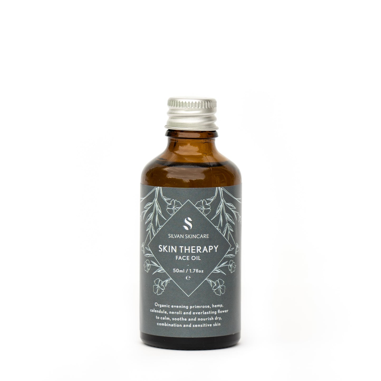 Silvan Skincare skin therapy Face Oil refill bottle. The facial oil is inside an amber glass bottle with a silver aluminium screw top. The bottle has a blue label, white text listing the product and brand and light blue botanical illustrations.