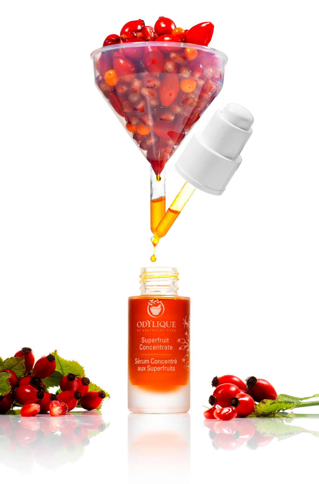 Odylique Superfruit Concentrate Organic Serum. A 30ml glass bottle featuring a white pump, positioned beside a funnel pouring rosehip and other vibrant botanics into the bottle