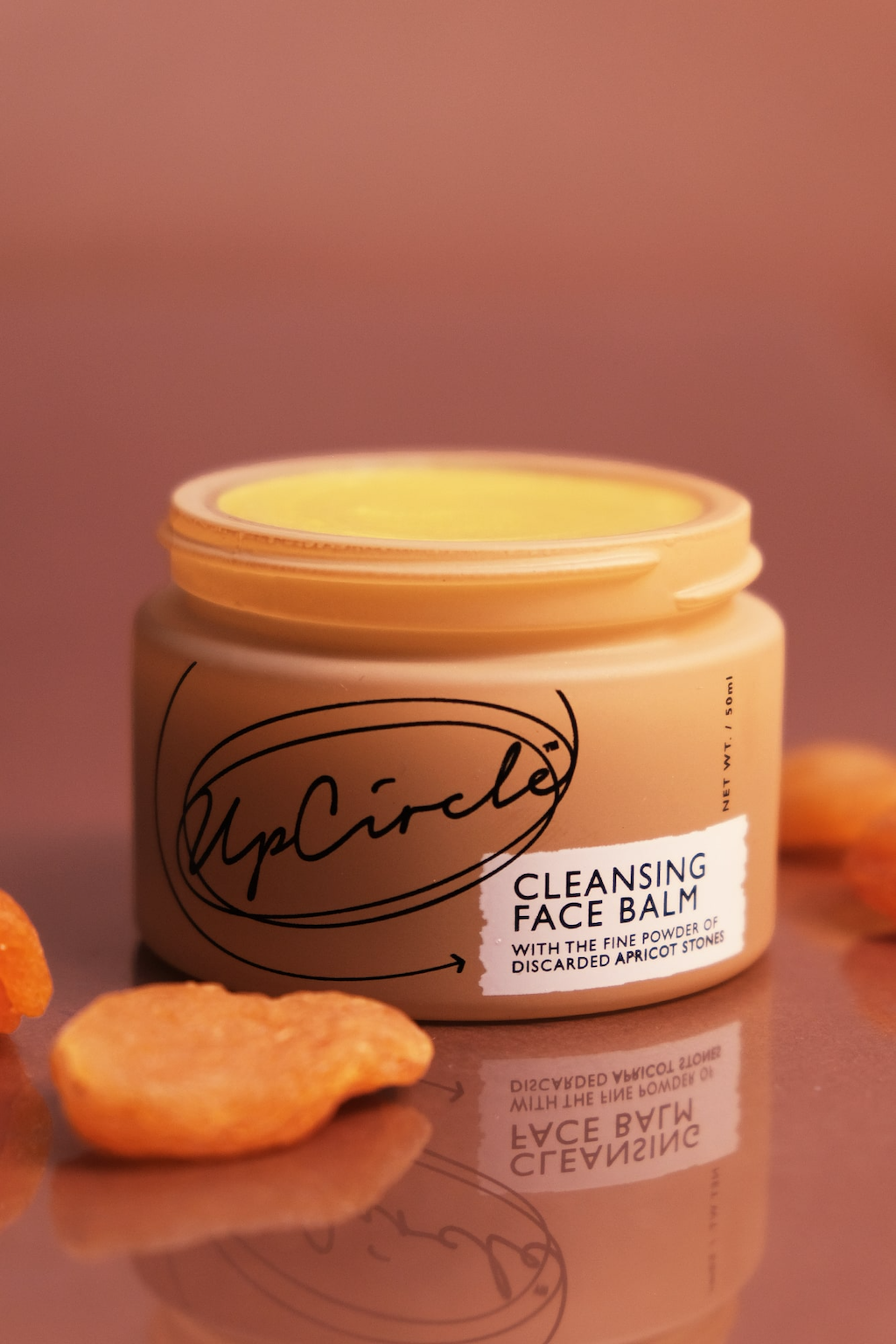 UpCircle Cleansing Face Balm. Sustainable skincare. The orange glass jar is sitting open against a dark pink background with some orange fruit slices sitting around it.