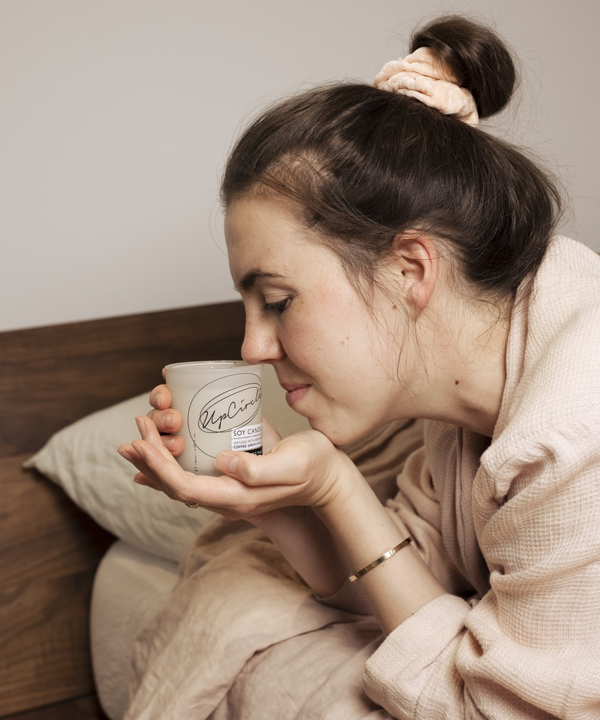 UpCircle Espresso Martini Soy Candle. Plastic free candle. A model is holding the candle in the palm of her hand and smelling it.