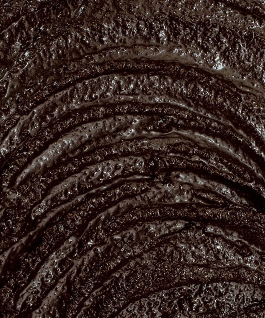 A close up shot of the body scrub showing the deep coffee colour and the hydrating, grainy texture.