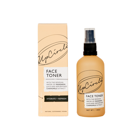 upcircle beauty face toner shot on a white background. on the left is the peachy orange box with black upcircle logo and a white label that reads 'face toner with the residual water of mandarin juice and repurposed chamomile extract - hydrate and refresh'. on the right you can see the orange glass bottle with the same logo and text and a black pump lid