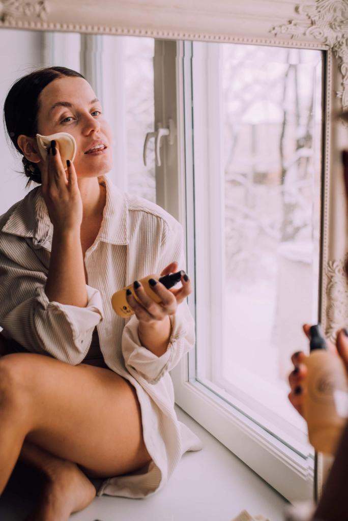 white woman sitting on a window sill is applying her upcircle toner using a reusable cotton pad