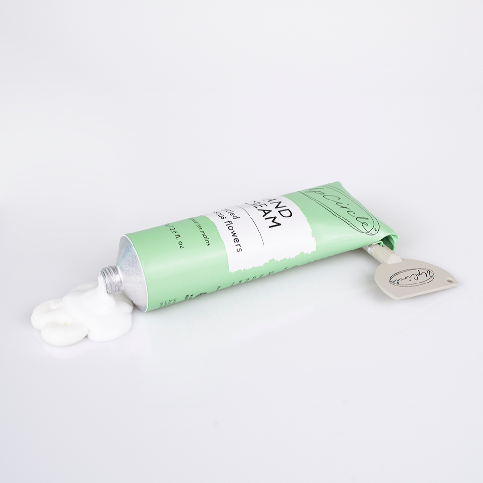 side view of the upcircle hibiscus hand cream which comes in a light green aluminium tube. you can see that the upcircle tube key squeezer has been used to roll down the aluminium tube in order to use every bit of cream and to dispense it. there is a large dollop of hand cream coming out of the tube