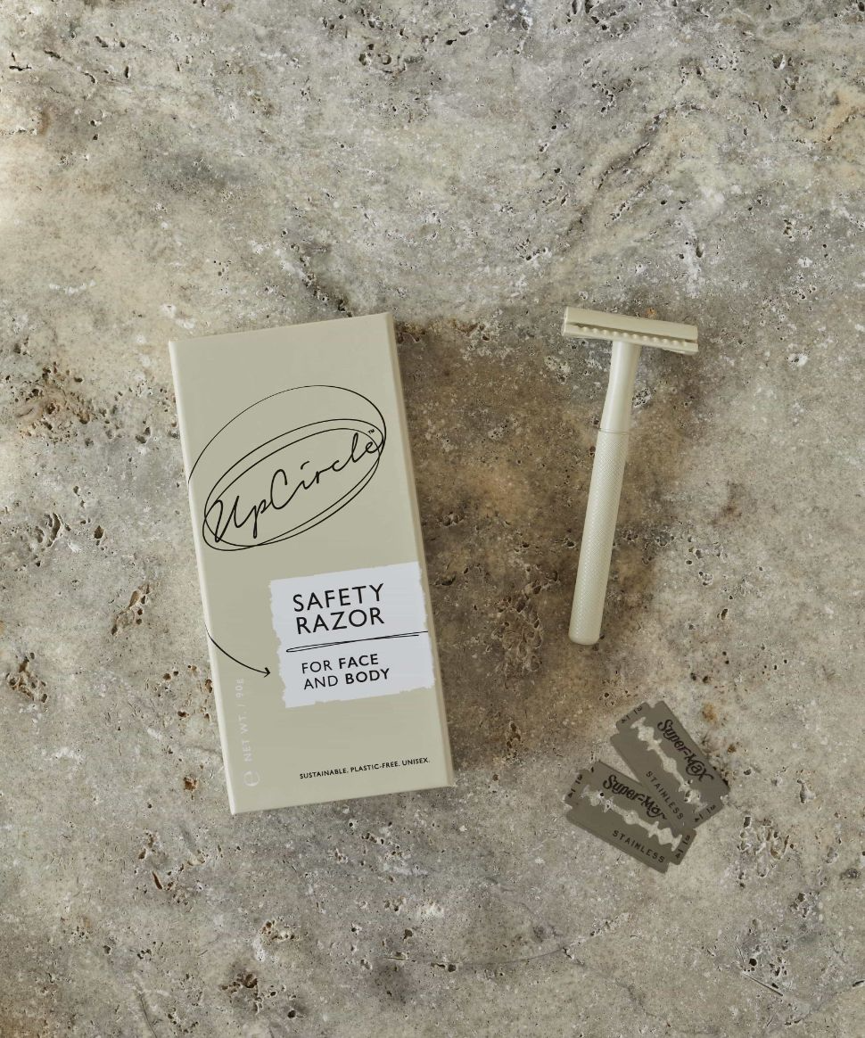 Flat lay of the upcircle safety razor on a textured grey and brown mottled surface. The box, the razor and 2 safety razorblades are pictured.