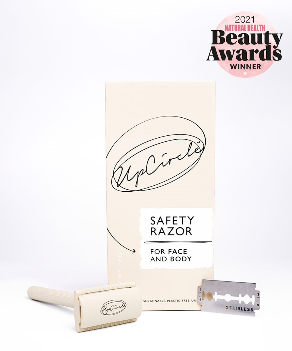 A beige UpCircle safety razor set is displayed. The packaging box reads "Safety Razor for Face and Body," and the set includes a razor handle and a detachable blade. A circular "2021 Natural Health Beauty Awards Winner" emblem is visible in the top right corner.