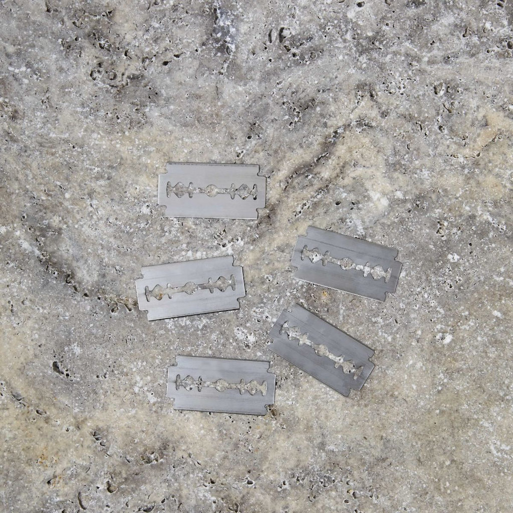 5 razorblades laid flat on a textured grey and brown mottled surface.