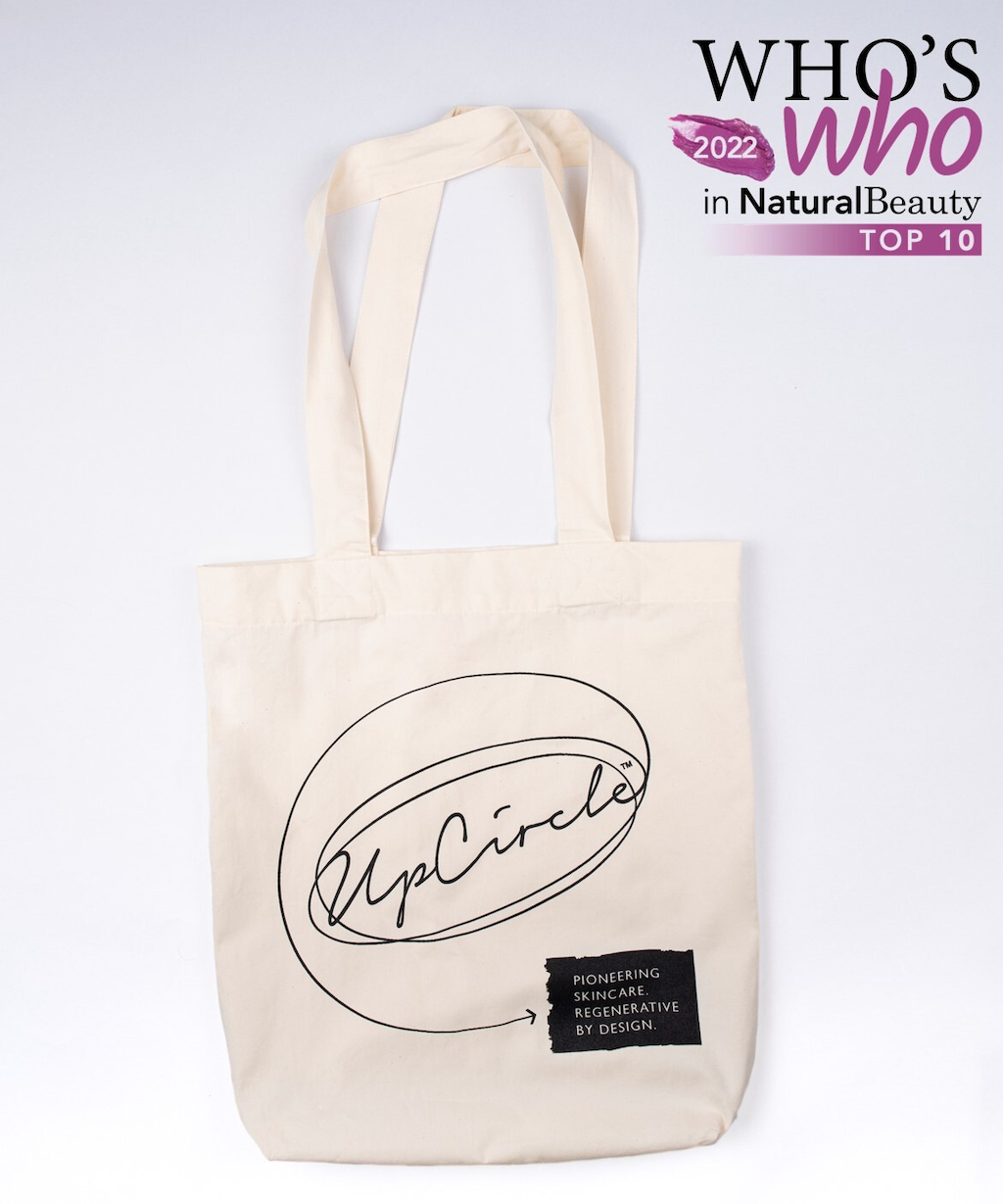 An image of the upcircle tote bag made from cotton and beige coloured. The brand name is printed in black. An sticker above "2022 Who's who in natural beauty"