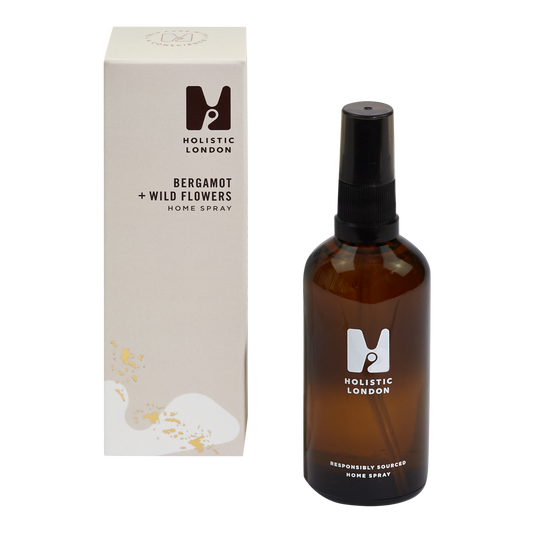 photograph of holistic london's bergamot + wildflowershome spray on a white background. on the left side of the image is the light purple cardboard box with the holistic london logo on it. the label reads ' bergamot + wildflowers homespray’. on the right side of the photo is the amber glass bottle with a black atomiser and lid which holds the spray. the glass is printed with the holistic london logo and says 'responsibly sourced home spray’