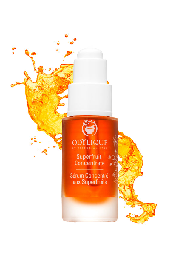 Odylique Superfruit Concentrate Organic Serum. Ethically sourced skincare. A 30ml glass bottle featuring a white pump, positioned in front of a burst of vibrant orange serum in the background.