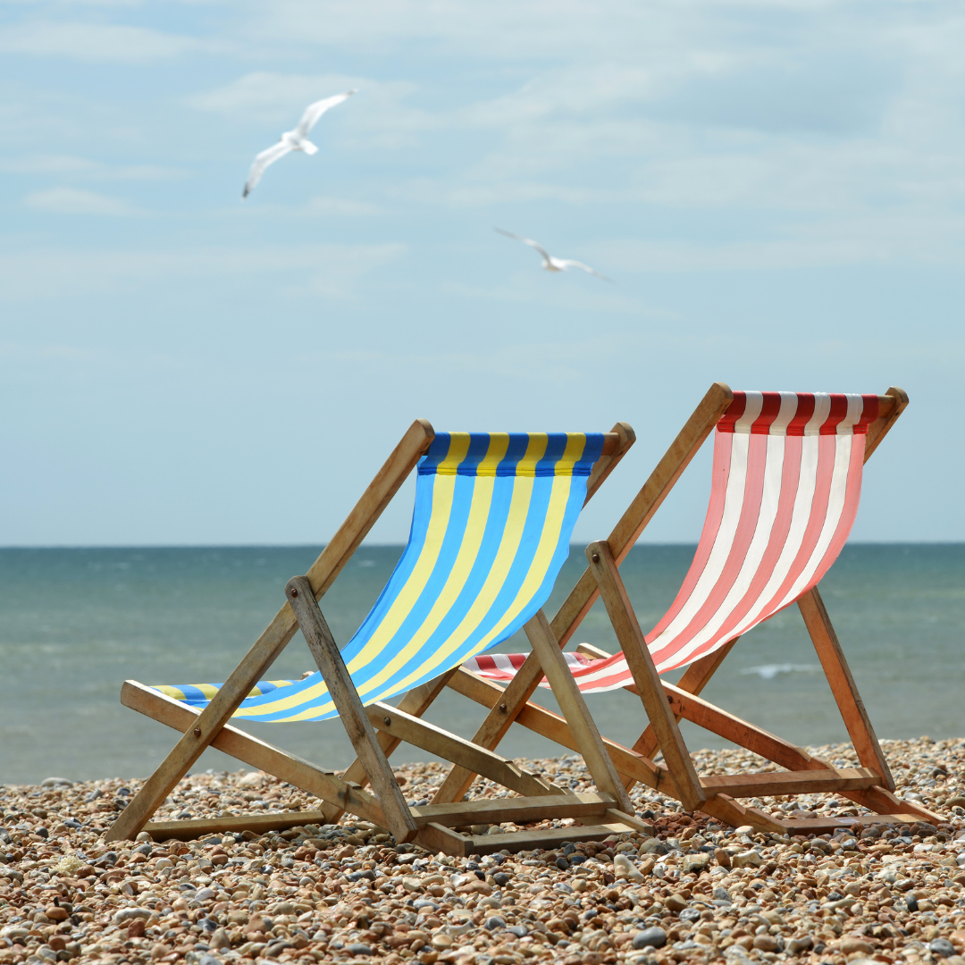 two deckchairs on a pebble beach blowing in the breeze one is blue and yellow striped and one 