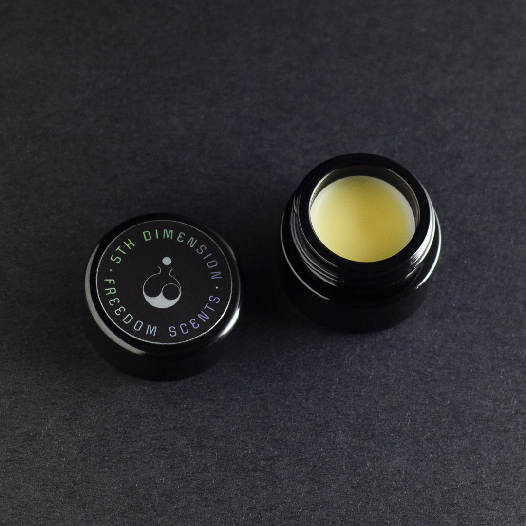 jar of solid perfume on a dark grey background with lid open and light creamy perfume balm inside