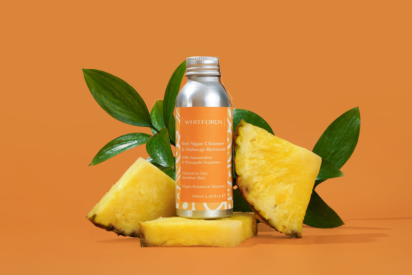 cleansing oil and eye make up remover in aluminium bottle with orange label on an orange background with pineapples surrounding it