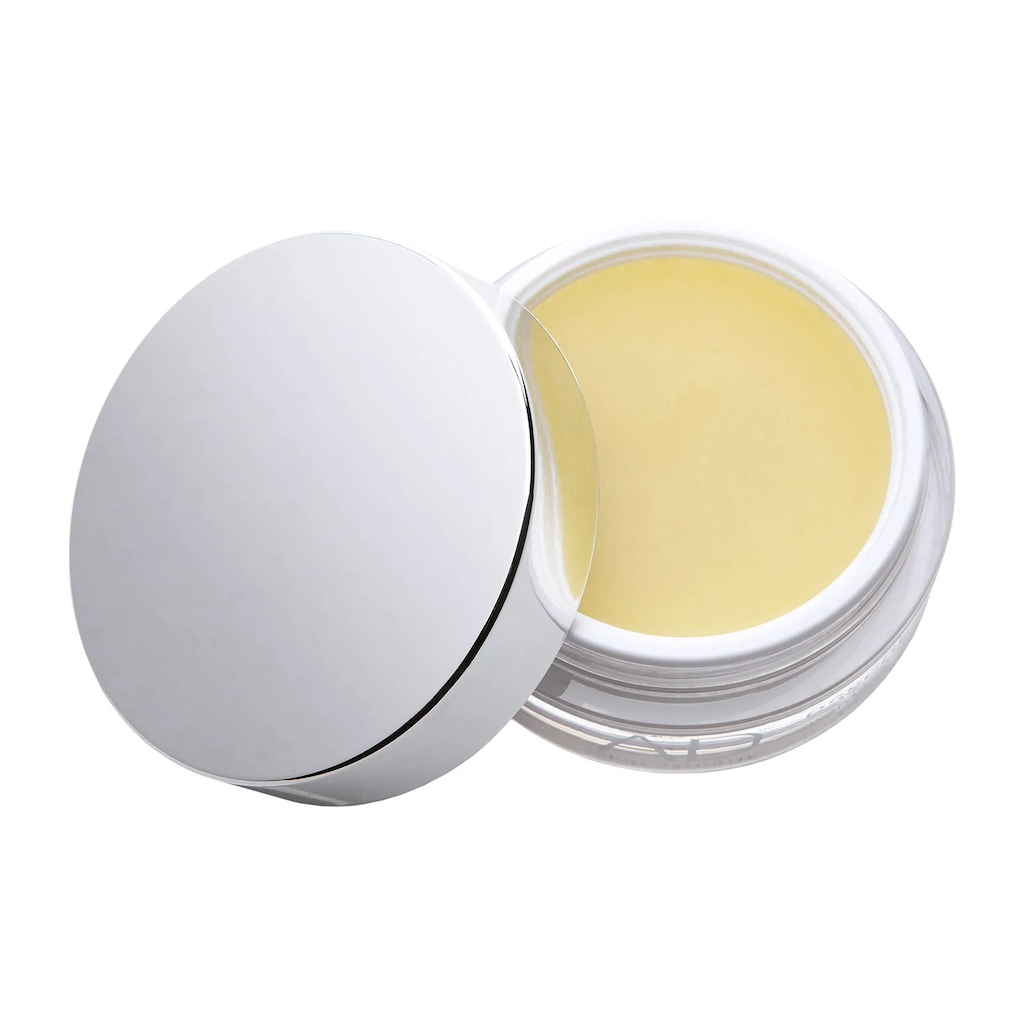 ad skin synergy cleansing balm texture which can be seen inside the clear acrylic pot. the silver lid is resting on the side of the pot. the cleansing balm has a creamy yellow colour and smooth texture