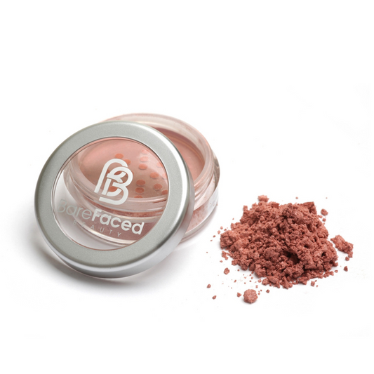 A small round pot of mineral blusher, with a swatch of the powder next to it showing a subtle satin, medium peachy pink shade