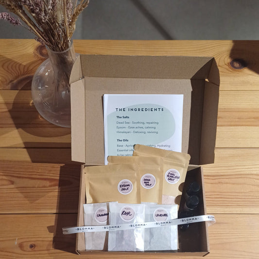 aerial view of brown box containing ingredients to make your own bath salts. salts, dried flower petals and base and essential oils in paper sachets and small glass bottles