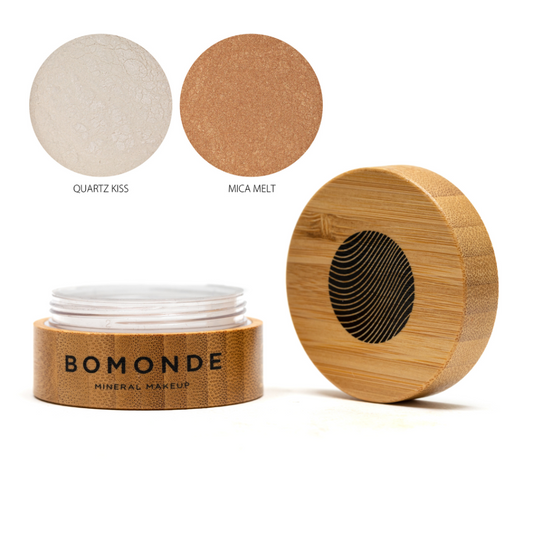 A round bamboo pot of Bomonde highlighter powder, lid unscrewed and placed upright next to the pot - two swatches in the top right corner in shades Quartz Kiss and Mica melt