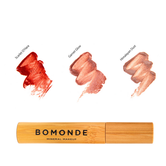 Flat lay of Bomonde Natural matte lipstick in the bamboo light brown packaging with 3 colour swatches above. From left to right; Scarlet O’Hara (shimmery red), Garnet Glow (shimmery pink), Himalayan Dust (shimmery light bronze).