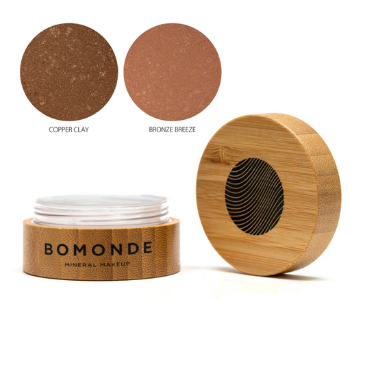 A round bamboo pot of Bomonde loose bronzing powder, lid unscrewed and placed upright next to the pot - two swatches in the top right corner in shades copper clay and bronze breeze