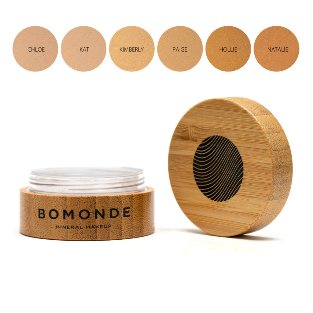 A round bamboo pot of Bomonde mineral foundation, lid unscrewed and placed upright next to the pot - six swatches displayed above the product from left to right; Chloe, Kat, Kimberly, Paige, Hollie and Natalie.