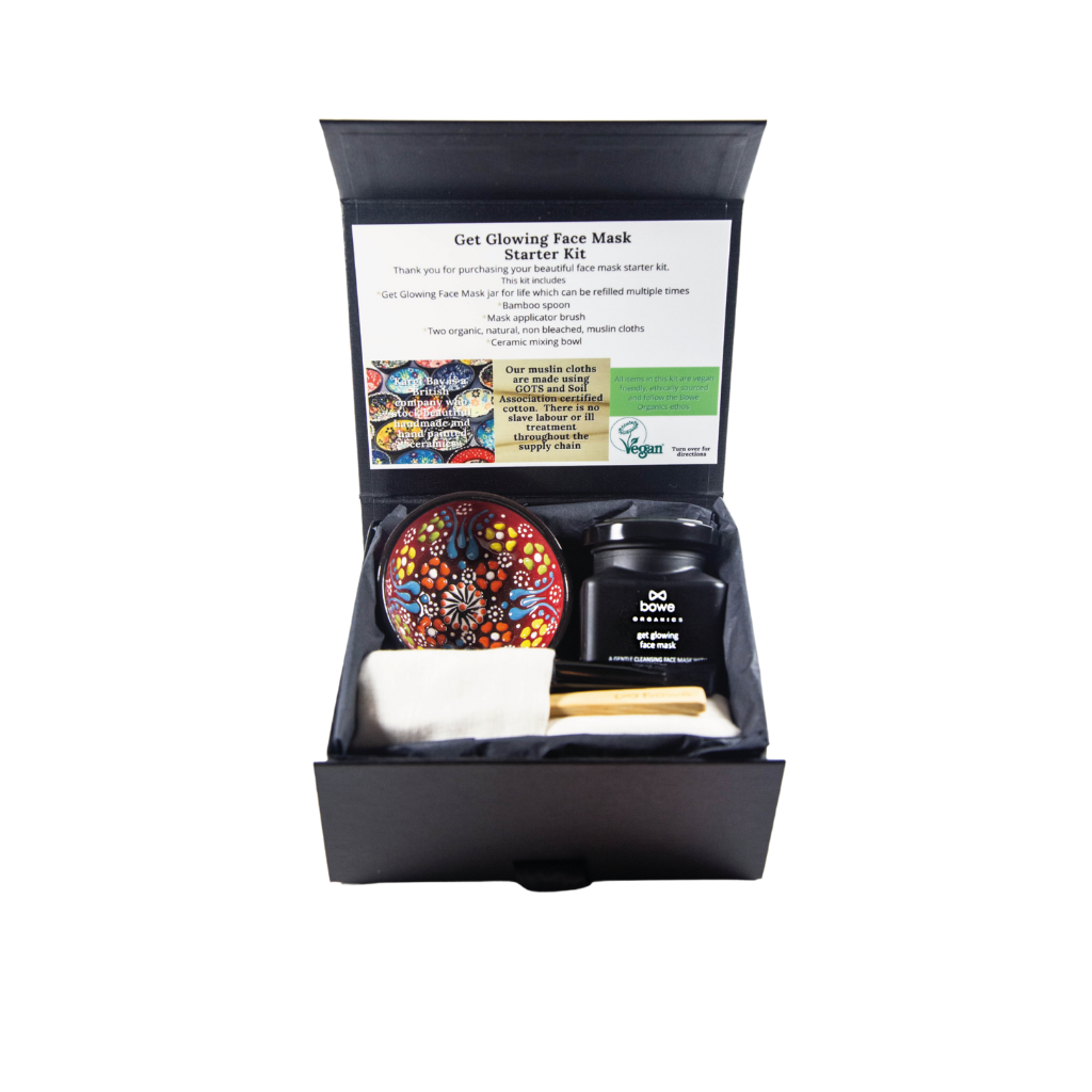 Black gift box with black tissue paper inside and contains a clay face mask gift set with a handpainted turkish style bowl a wooden mask mixing spoon, black face mask applicator brush, two organic cotton GOTS face cloths. Box is open and facing towards the camera