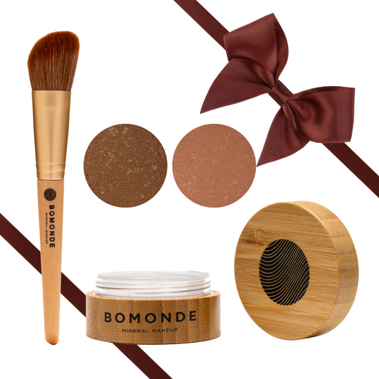 flat lay image of a bamboo handled synthetic bristled make up brush with brown satin effect ribbon angled on each corner. There are two swatches of bronzer in circles and underneath there is a bamboo pot with the lid next to it