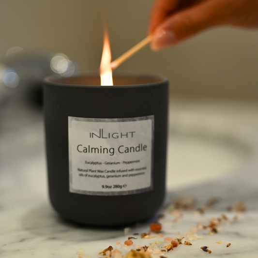 Inlight calming candle being lit with a match on a marble surface and dried flower buds in the foreground