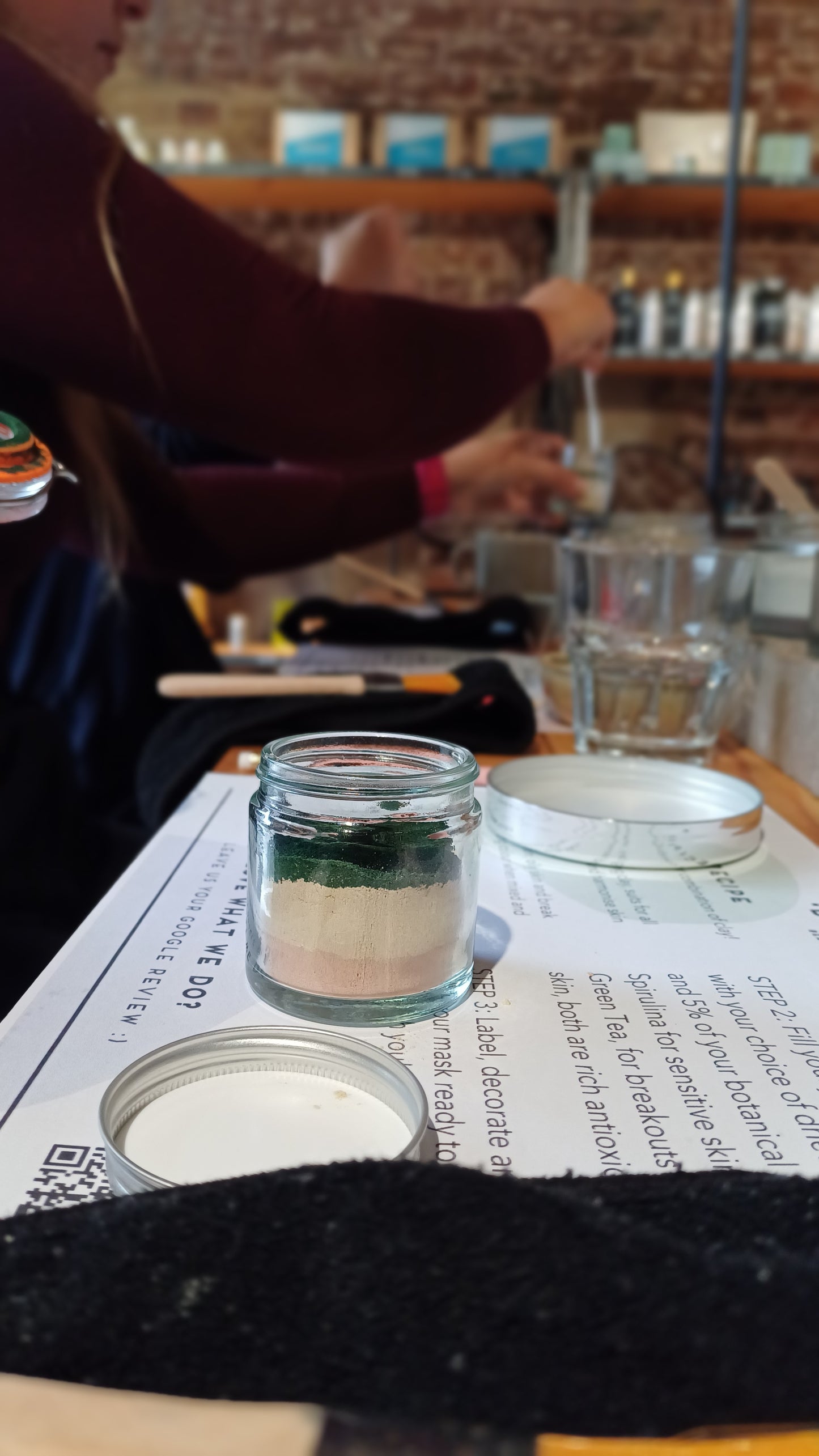 photo of our make your own skincare workshop in the middle of a class. on the table you can see the instructions, head band and face mask brush sitting along side a clear glass jar containing a blend of different clays used to create your own clay based face mask