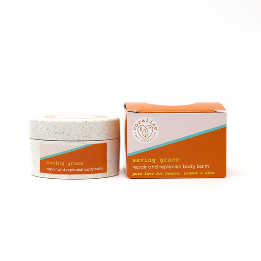 A round container of “saving grace” repair and replenish body balm sits next to its matching box. Both the container and the box have an orange and white design with text that reads, “pure love for people, planet & skin” along with a logo.