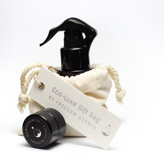 Freedom scents mood mist room pillow and linen spray black pump spray bottle placed in a cotton bag with a white tag that reads ‘eco-luxe gift bag’ by freedom scents. Placed in front, is a pot of the solid perfume.