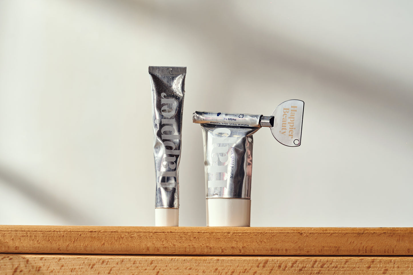 natural whitening toothpaste in a recyclable aluminium tube. On the left is the travel size and on the right is the full size which is partially used and so a tube key roller is used to roll up the tube.