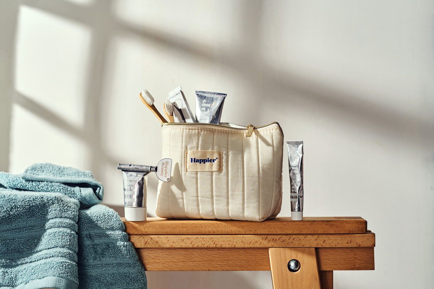 lifestyle image of happier beauty natural dental products sitting in a creamy fabric washbag on a wooden bench