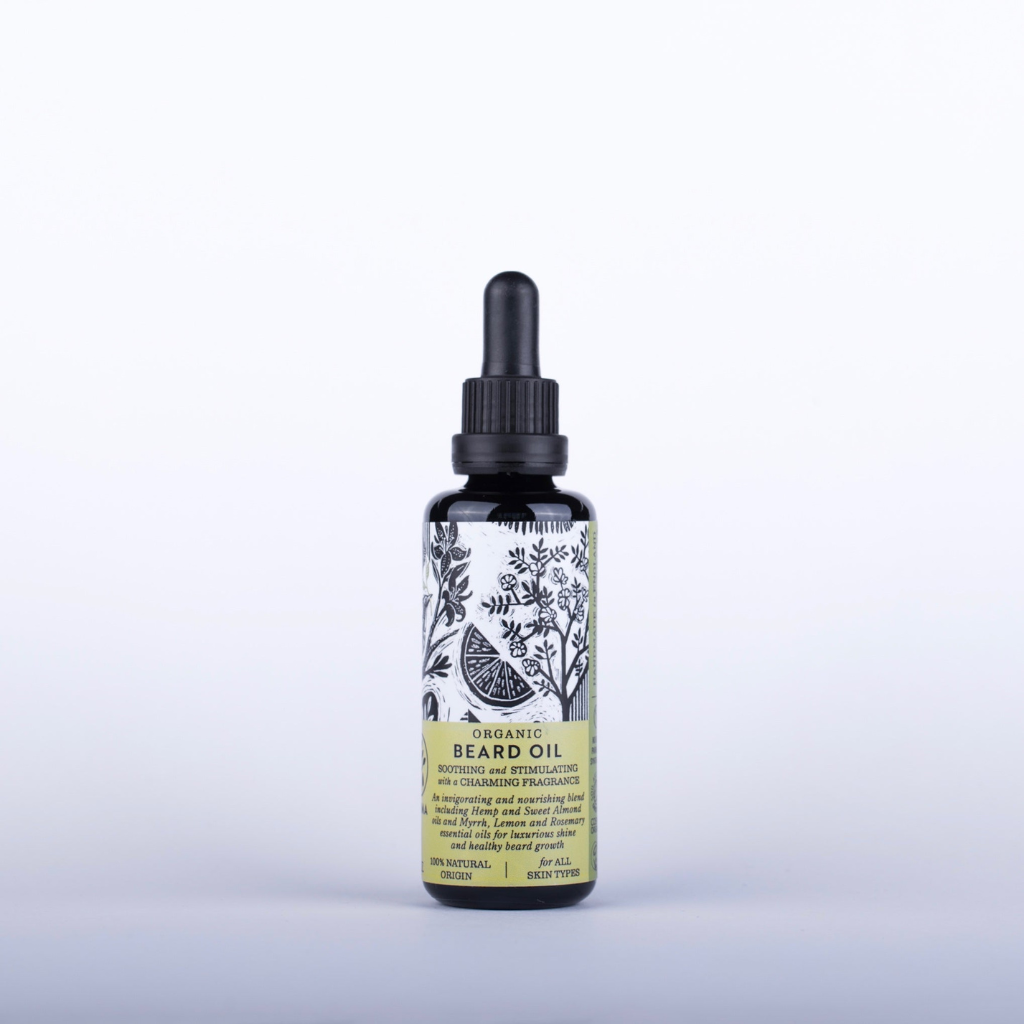 A black, dropper-top bottle of the ham organic beard oil against a plain white background. The label features botanical illustrations, yellow accents, and reads "Beard Oil" along with some descriptive text about the product ingredients and benefits.
