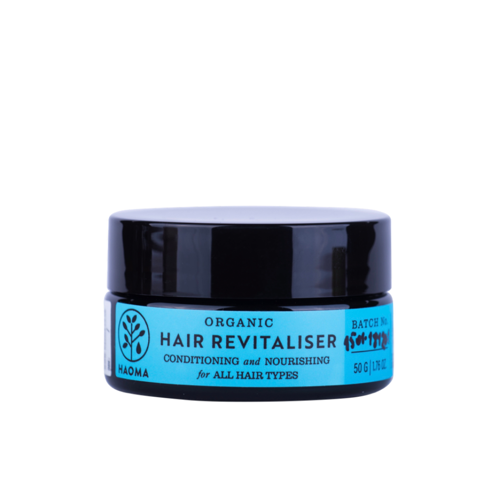 A jar of haoma Organic Hair Revitaliser. The jar is dark with a blue label that reads, "Conditioning and Nourishing for All Hair Types, 50g, 1.7 oz.” with a small tree logo
