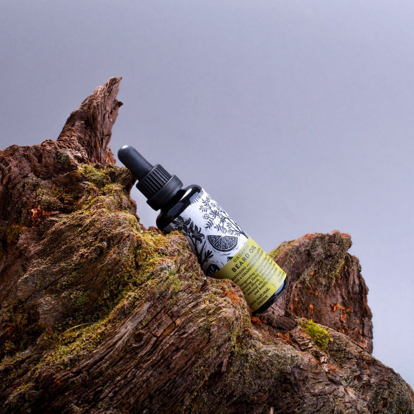 beard oil bottle on moss covered tree bark