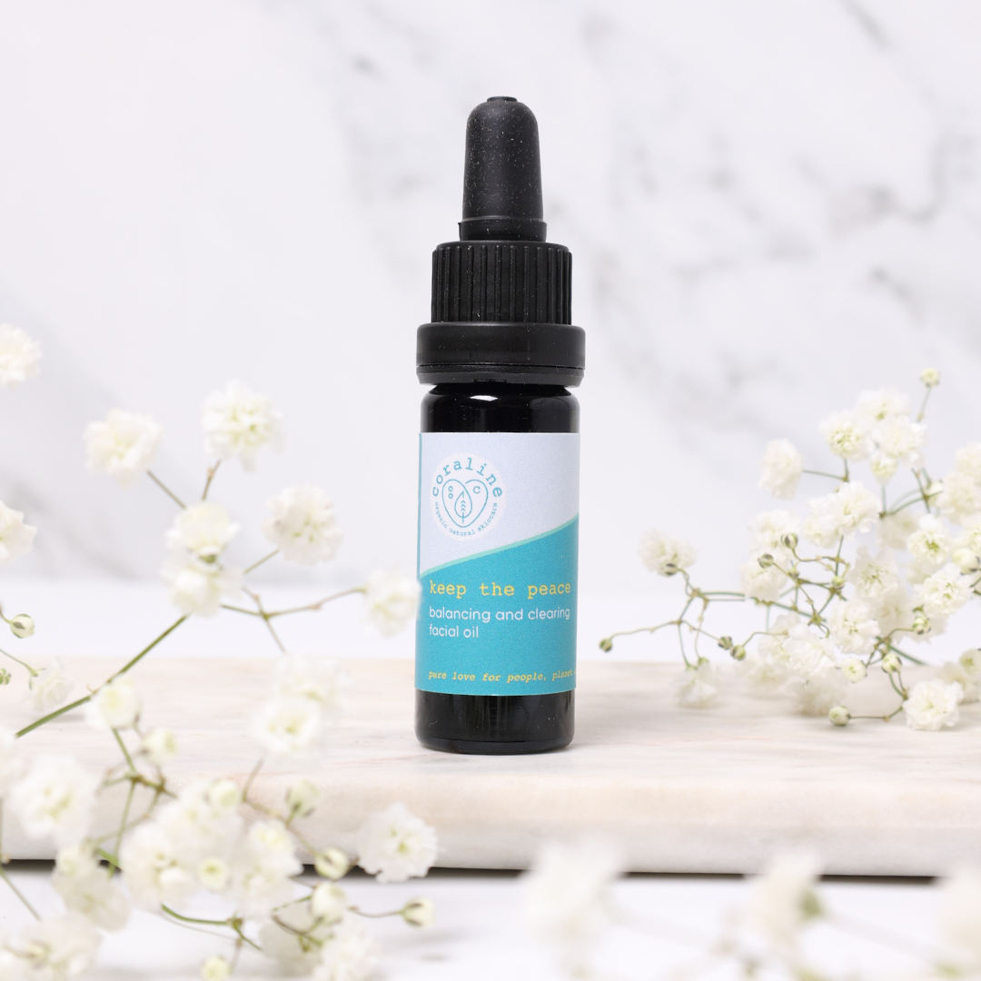 photo of the travel sized keep the peace face oil nestled between gysophilia flower buds and sitting on top of a white marble slab. the organic face oil comes in a black glass bottle with a pipette lid