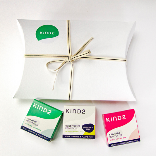 Natural and plastic free gift box of the Kind2 Discover Bar Bundle. Pictured a white box with a cream coloured ribbon and a KIND2 sticker. Underneath, three small square boxes of the shampoo bars included in the bundle (left to right: the rebalancing one, the conditioner and the hydrating one)