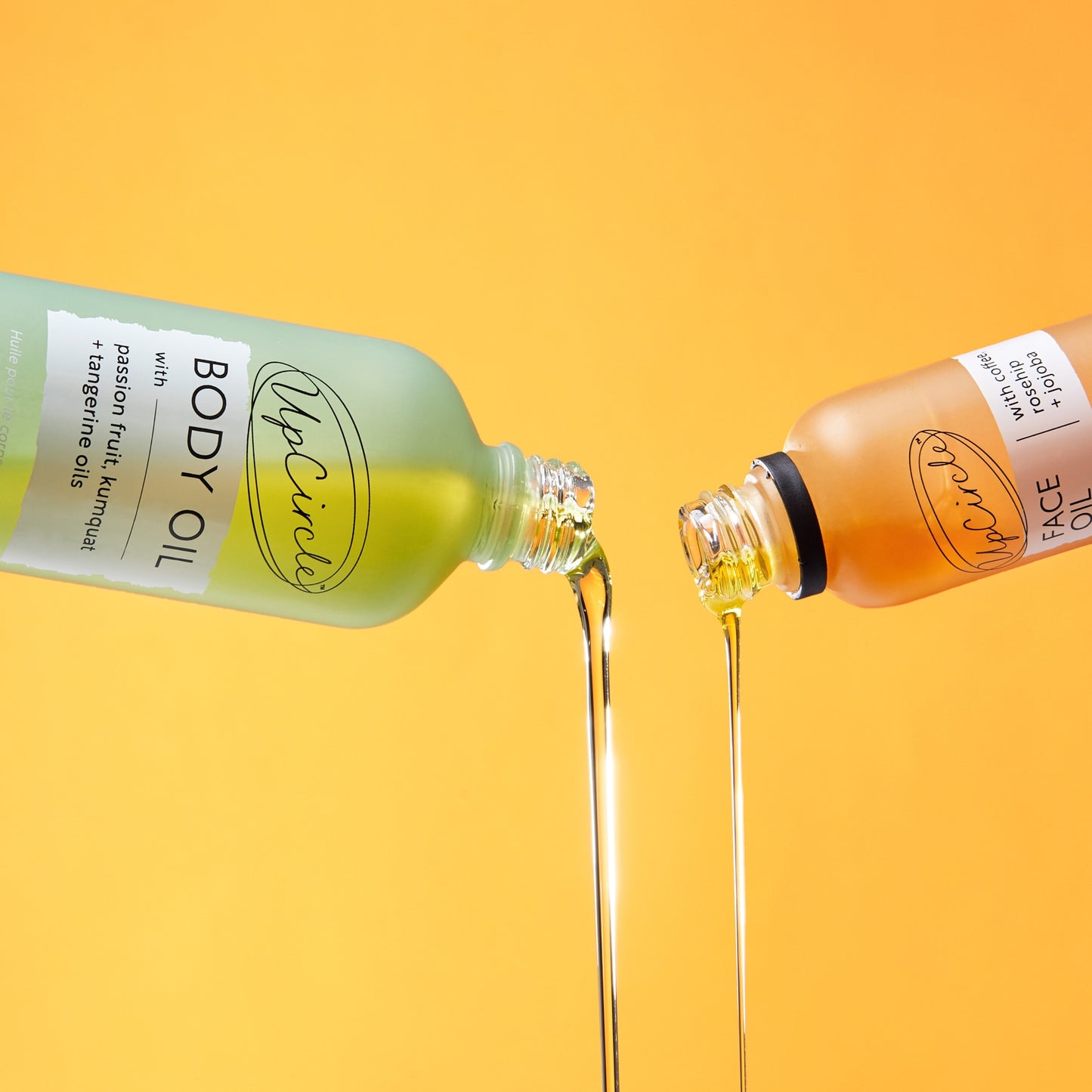 image of upcircle body oil and face oil being poured out of their respective green and orange bottles on an orange background