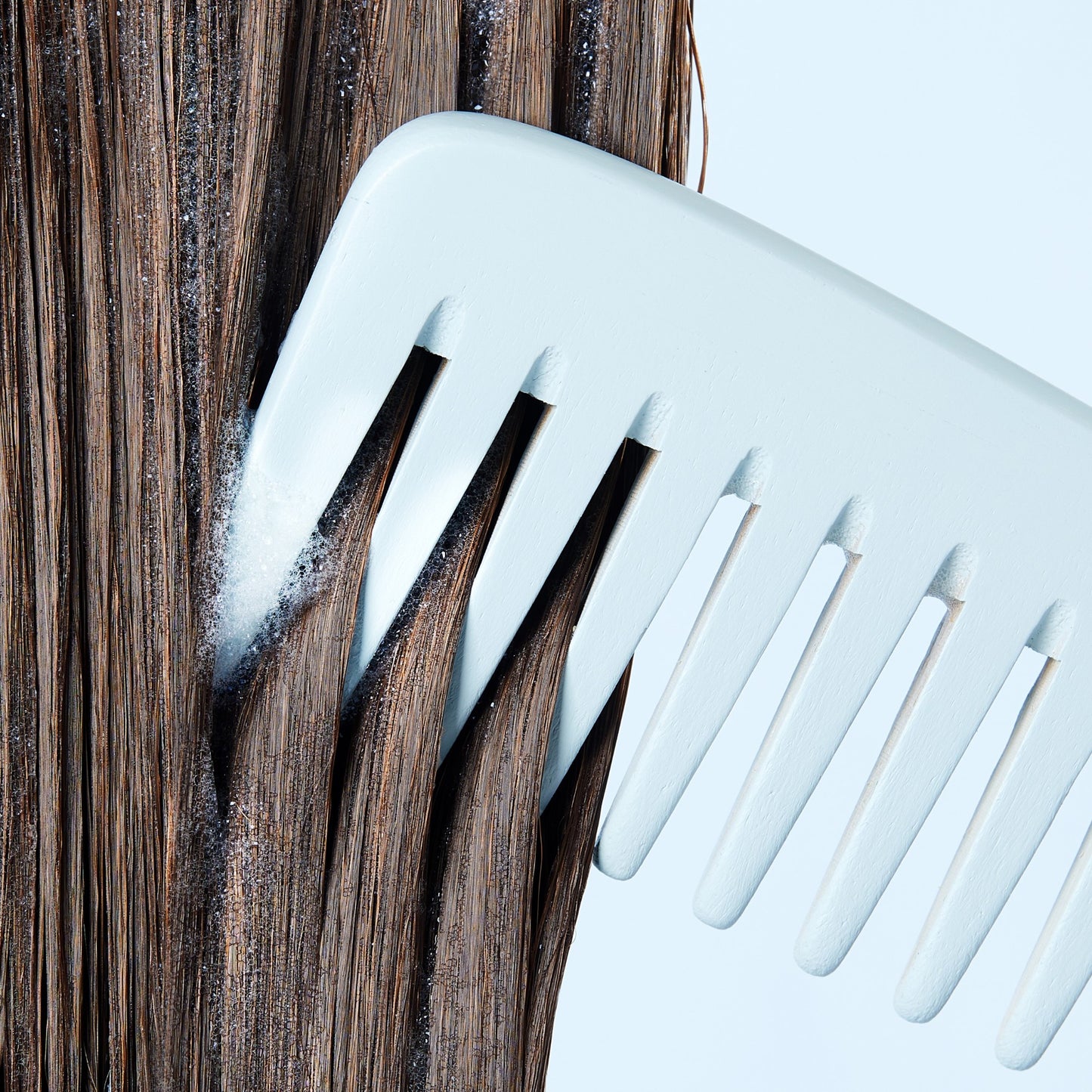 close up of upcircle bamboo wide toothed comb being brushed through damp brown hair