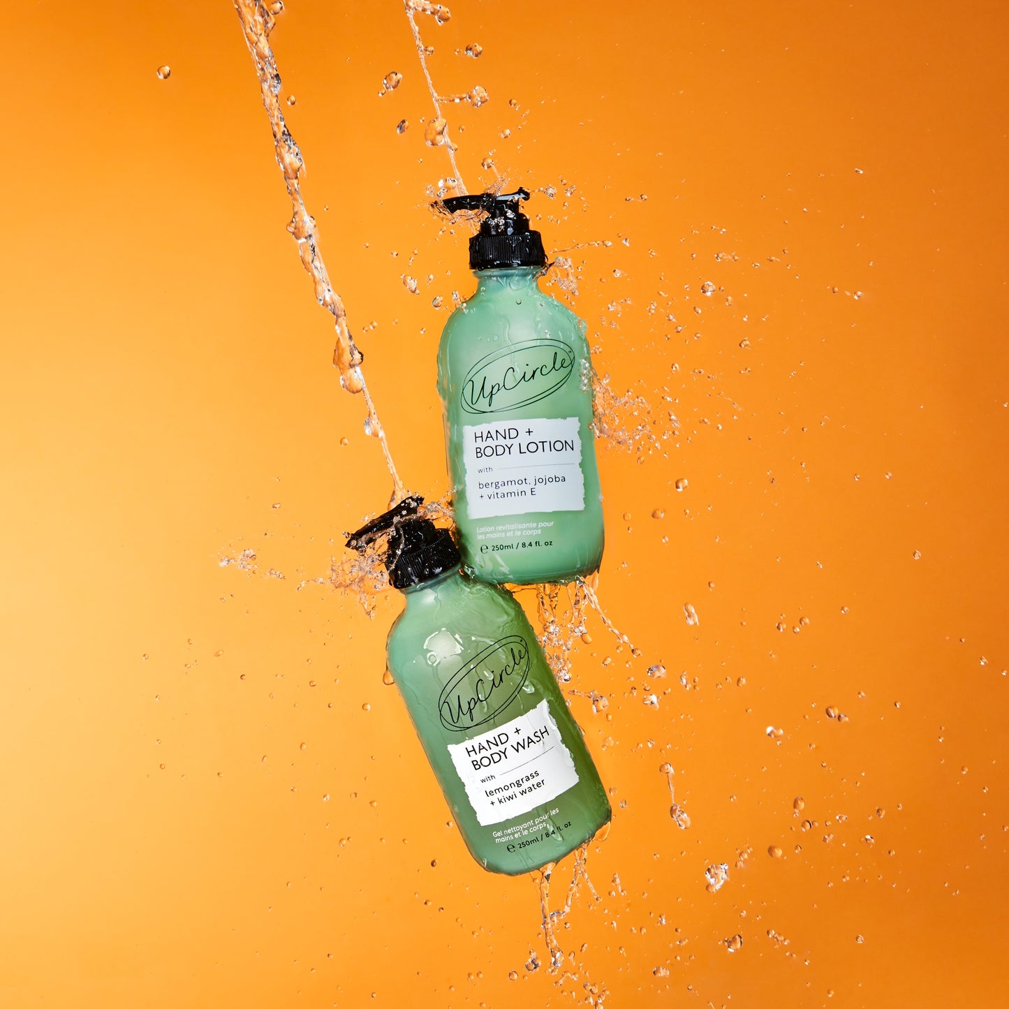 upcircle green frosted glass bottles of bodycare products on an orange background being drenched in water