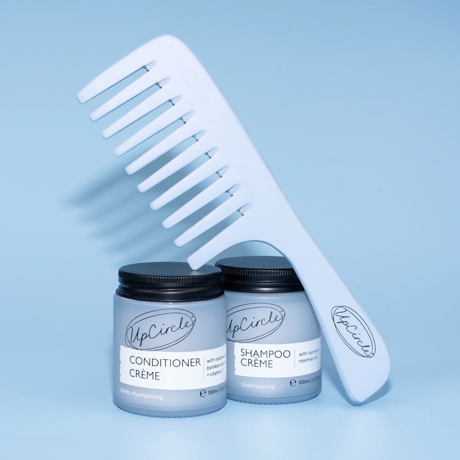 upcircle wide toother bamboo comb with handle propped up against their blue glass jars of concentrated shampoo and conditioner cream