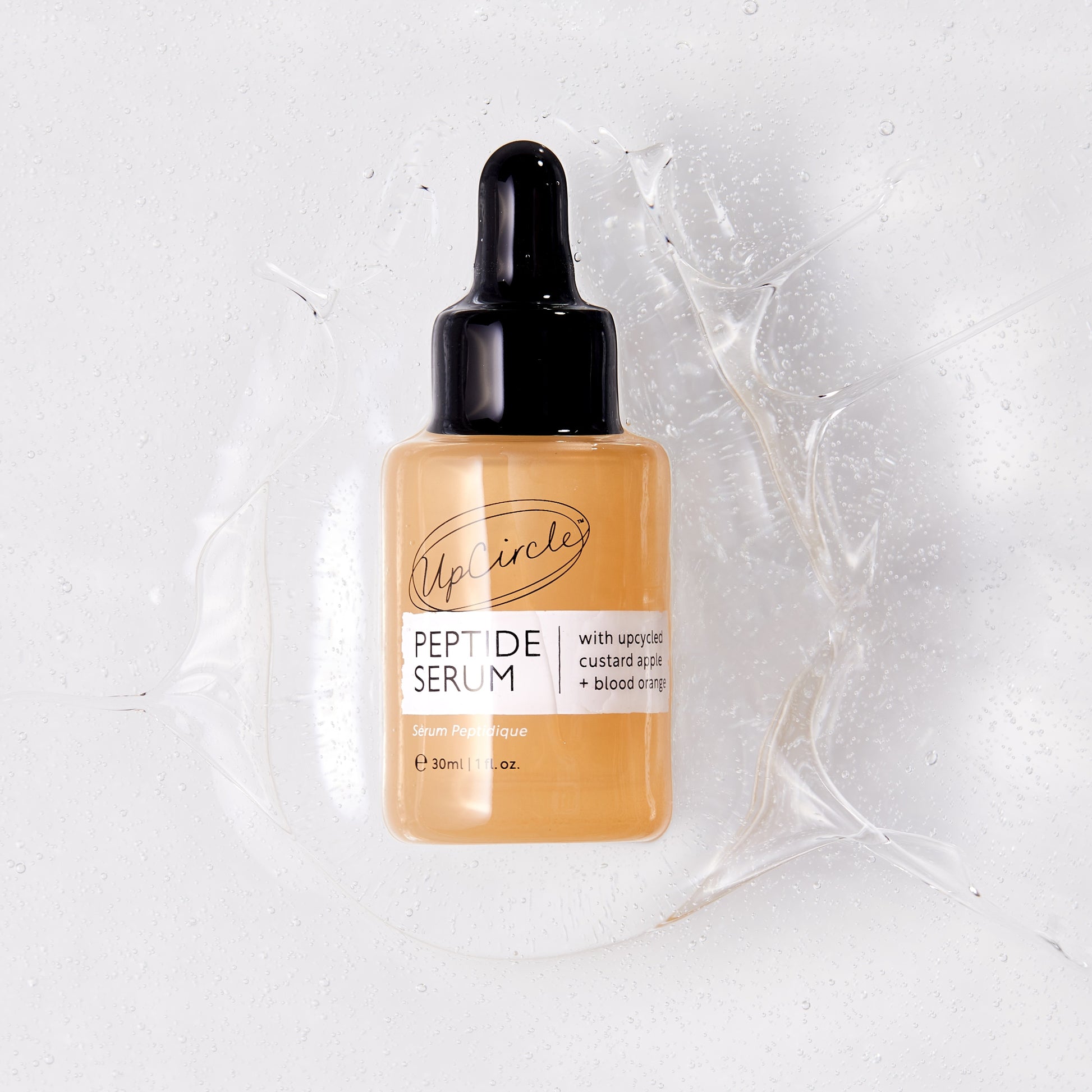 upcircle peptide serum in orange glass bottle with black pipette suspended in the texture of the serum