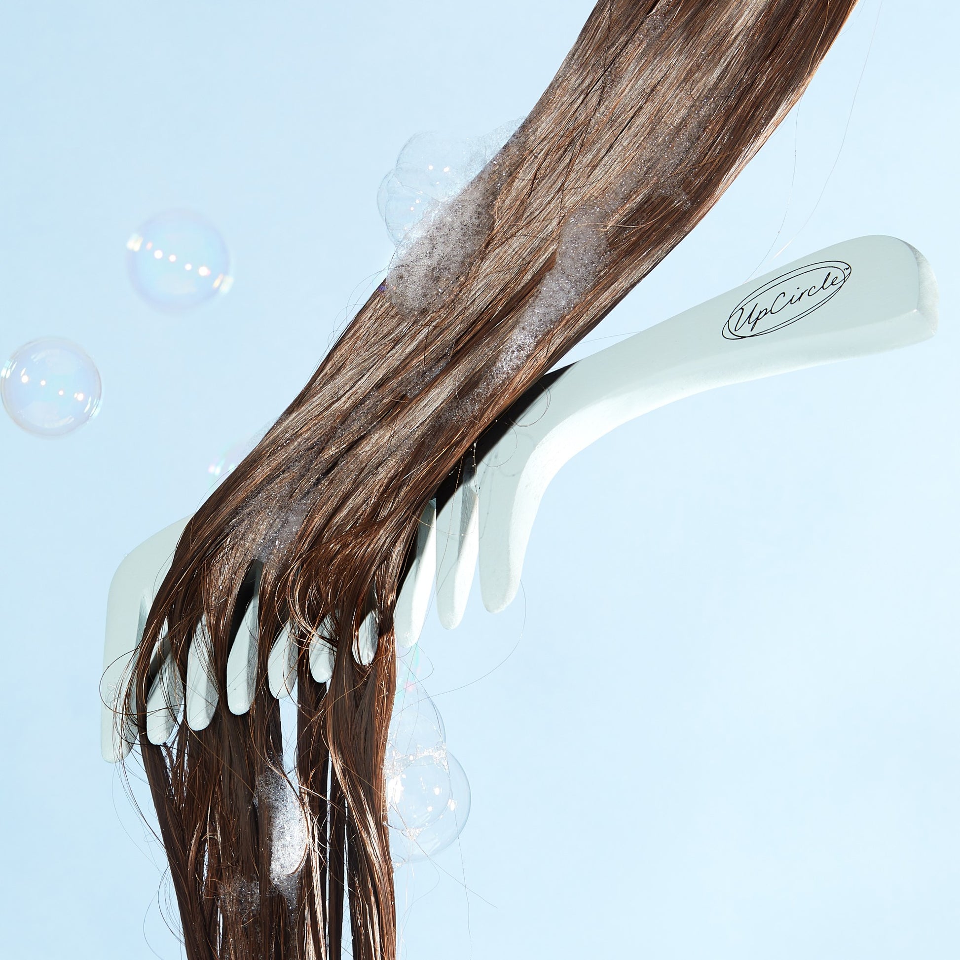 upcircle blue bamboo wide toothed comb being combed through a section of wet brown hair with suds in it