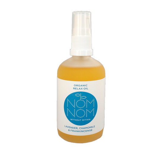 photo of nom nom's organic relax oil, a multipurpose natural oil blend for face and body. The bottle of oil is on a white background. the bottle is a slightly frosted bottle but you can still see the yellow coloured botanical oils inside it. the bottle has a plastic pump lid and a white label with blue accents. the label reads ' organic relax oil. nom nom without within, lavender chamomile and frankincense' 