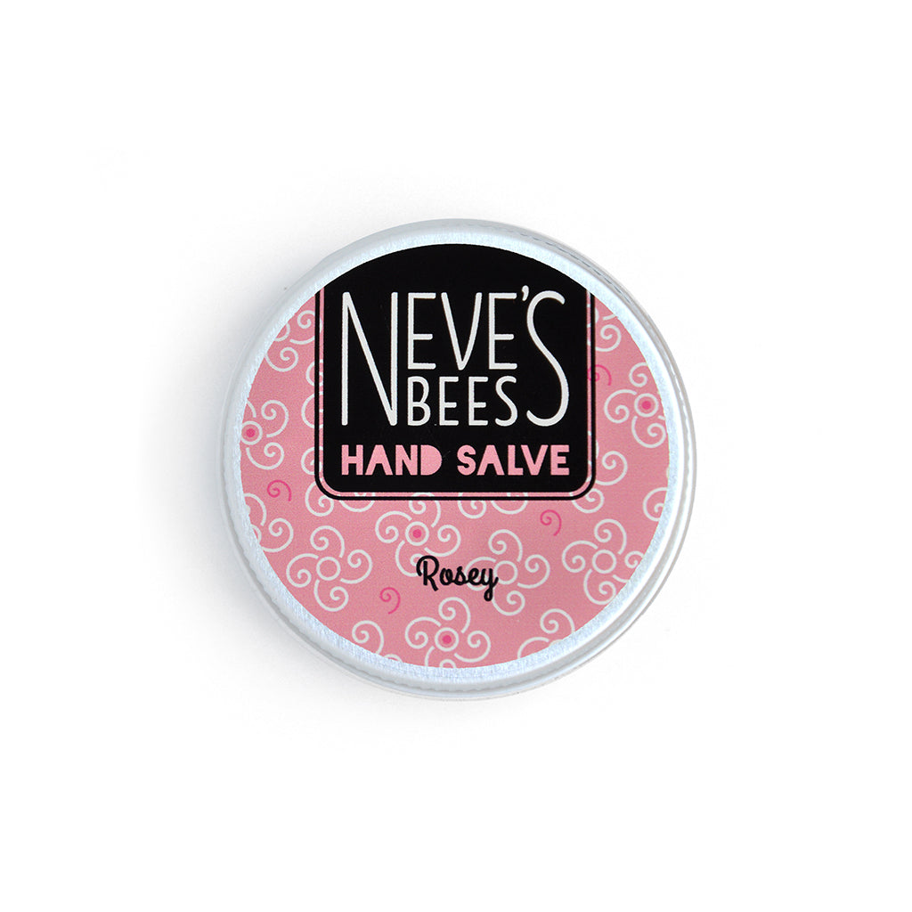 photo of neve's bees hand salve on a white background. the hand salve comes in an aluminium tin with a rose pink label on it that reads 'neve's bees hand salve rosey' there are graphics of swirly flowers in the background of the label