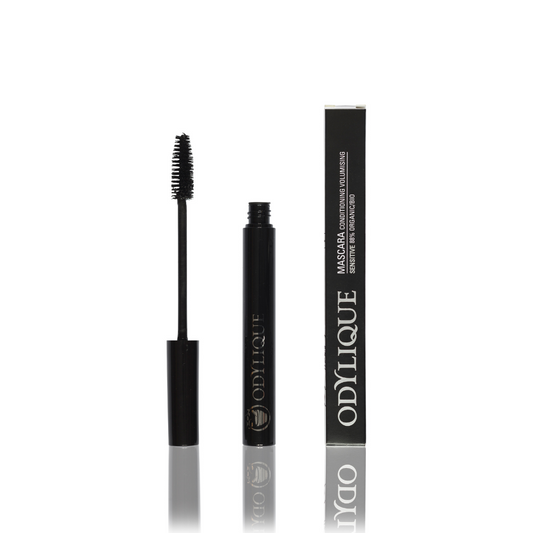 An image of an open mascara tube with its brush displayed to the left. next to the tube, its black packaging box with "odylique" logo in white text. plain white background enhances contrast.