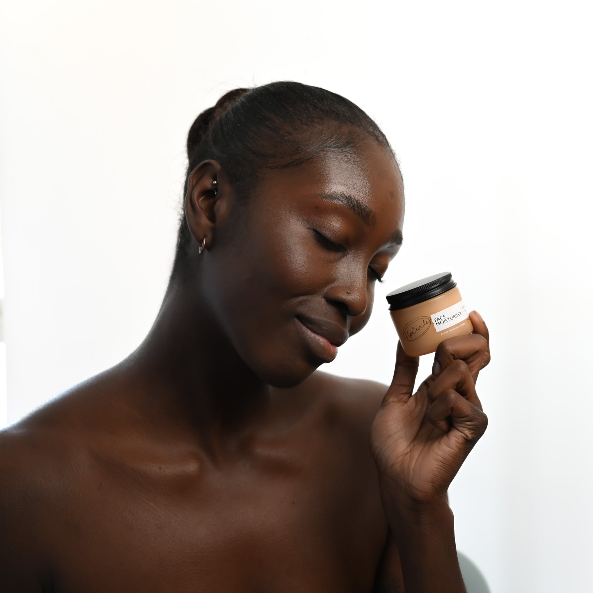 black woman smiling as she holds the upcircle moisturiser from the day and night hydration kit