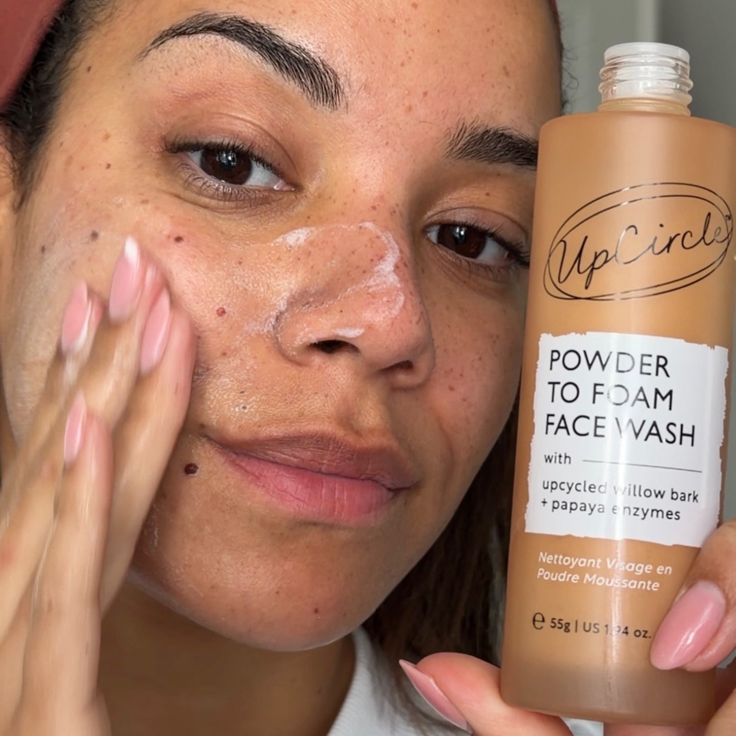 Person applying facial wash to their face with a bottle of UpCircle's Powder to Foam Face Wash.