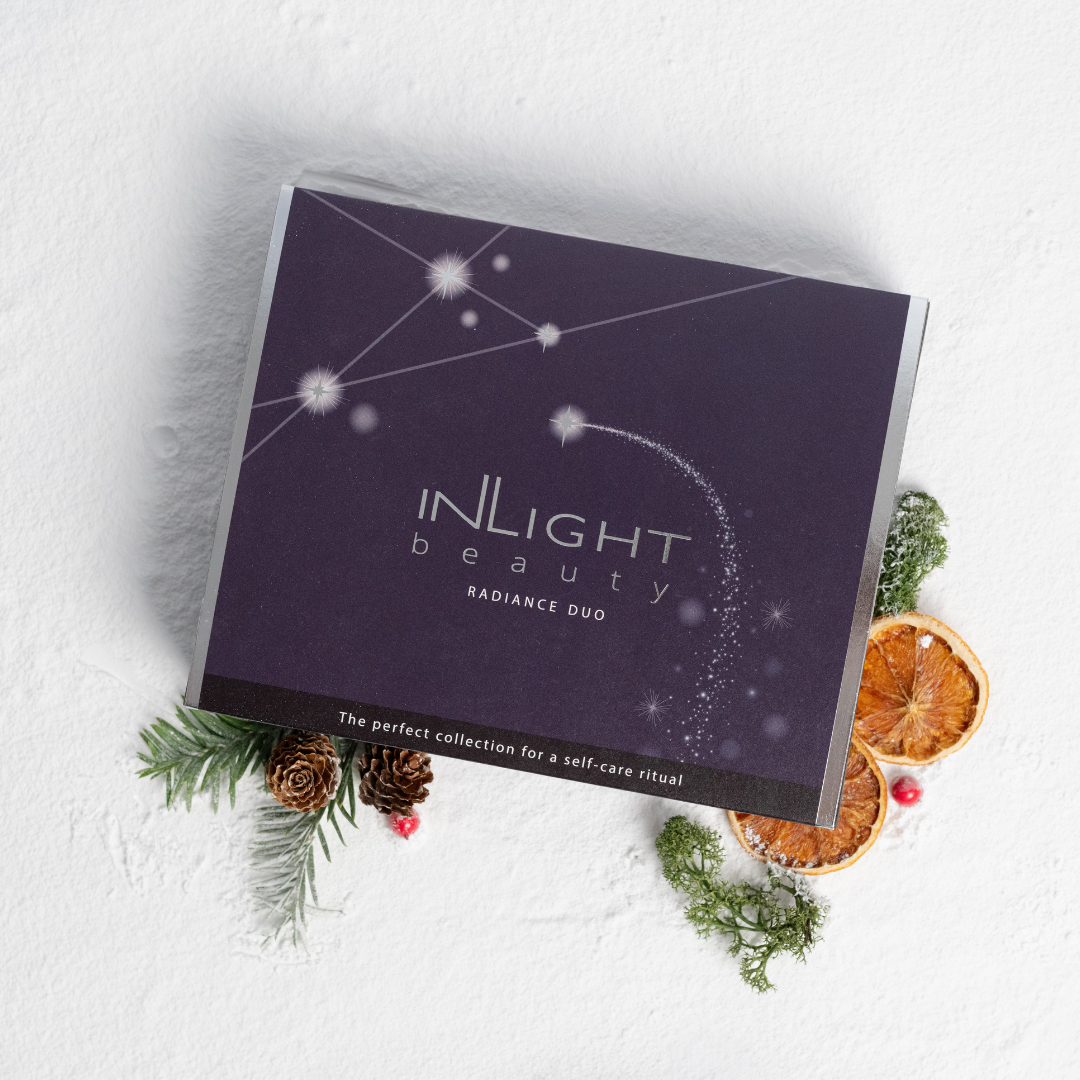 purple gift box containing inlight beauty's radiance dup - the perfect collection for a self-care ritual. underneath the box are festive elements like sea moss, pine cones and dried oranges on a bed of snow